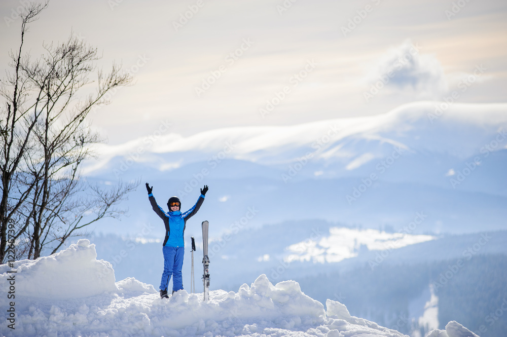 Happy skier standing on the top of the mountain with her arms lifted up against the background of beautiful winter mountains. Carpathian Mountains, Bukovel, Ukraine