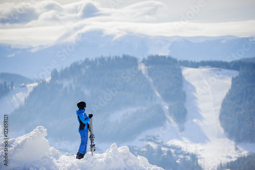 Rear view of skier standing on top of the mountain and enjoying the view on beautiful winter mountains on a sunny day. Winter sports concept. Ski resort
