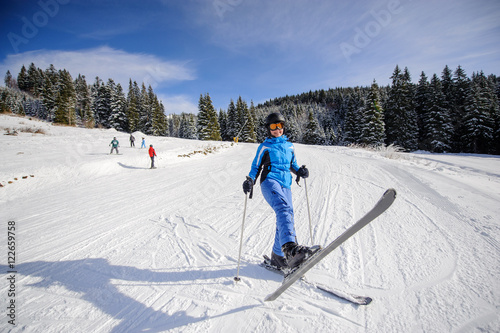 Wide shot of woman skier on a ski slope at ski resort on a sunny day. Winter sports concept.