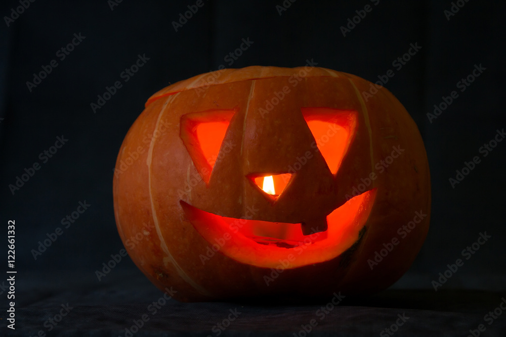 Creepy carved pumpkin face with a smile with a burning candle inside, on a dark background, selective focus Creepy carved pumpkin face with a smile with a burning candle inside, on a dark background, selective focus