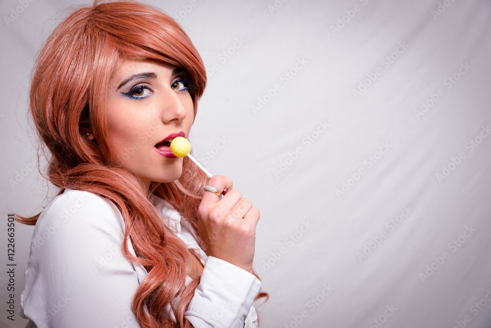 Ragazza con camicia bianca e capelli color pesca che mangia un lecca lecca Ragazza con camicia bianca e capelli color pesca che mangia un lecca lecca