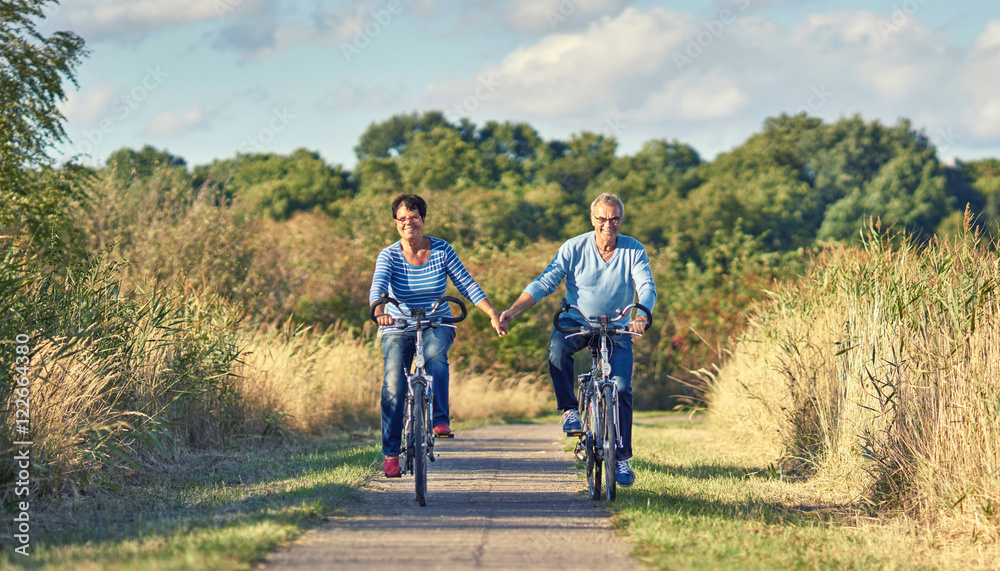 Senioren fassen sich bei der Hand beim Radfahren Senioren fassen sich bei der Hand beim Radfahren