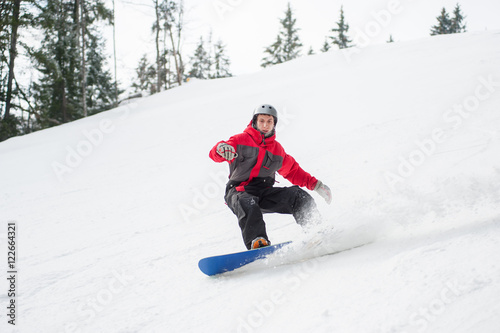 Young man snowboarder riding over the slope at the mountains. A ski run on the snowy slope below at a winter resort, extreme sport