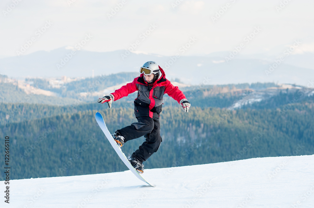 Cool man snowboarder riding on his snowboard and taking his for the edge on  top of a mountain against the backdrop of mountains, hills and forests in  the distance. Stock Photo