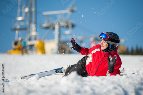 Smiling girl skier lying with skis on snowy at mountain top and throws snow in sunny day, having fun at a winter resort, ski lifts and blue sky in background. Bukovel, Ukraine
