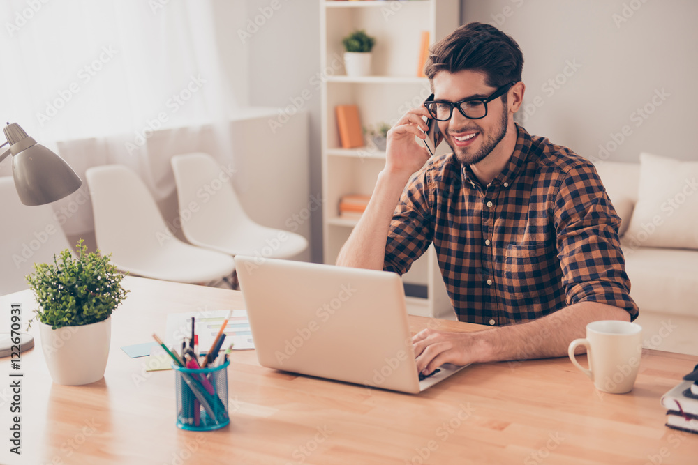 Young freelancer working with laptop and talking on phone with c
