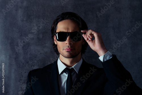 Portrait of serious bodyguard touching his black glasses