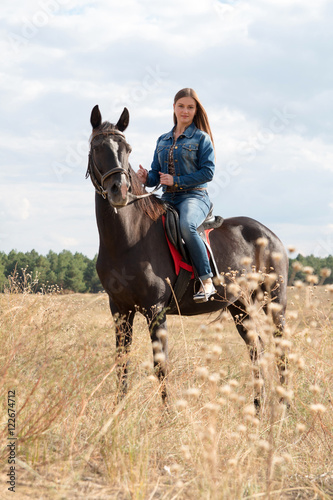 A young girl in a denim suit on a dark horse. © milogrodskiy