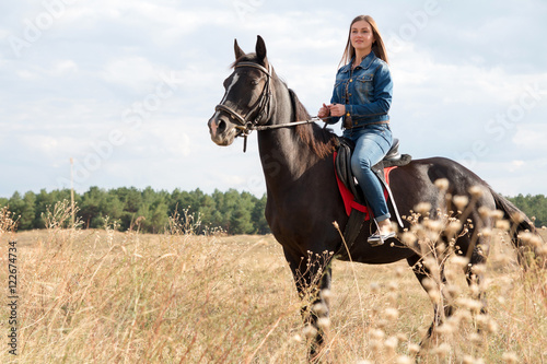 A young girl in a denim suit on a dark horse.