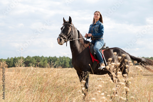 A young girl in a denim suit on a dark horse. © milogrodskiy