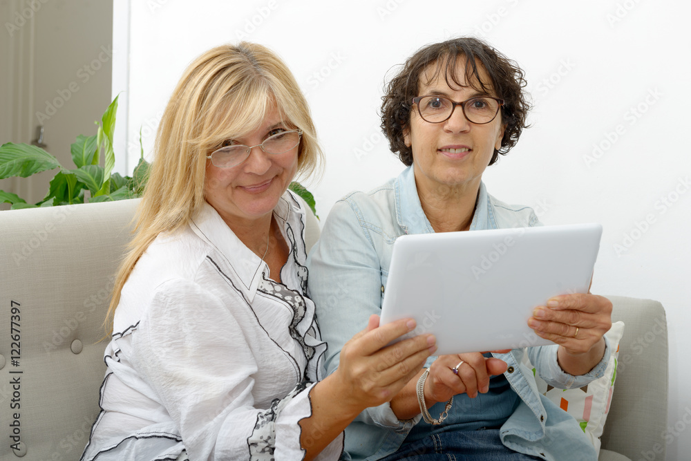 Two attractive mature women websurfing with tablet Two attractive mature women websurfing with tablet