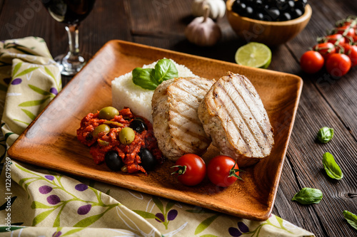 Grilled tuna steaks served with rice, tomato sauce with olives