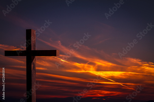     Jesus Christ cross. Christian wooden cross on a background with dramatic lighting, colorful sunset, twilight and orange -  purple clouds and sky.  Easter, resurrection,Good Friday concept