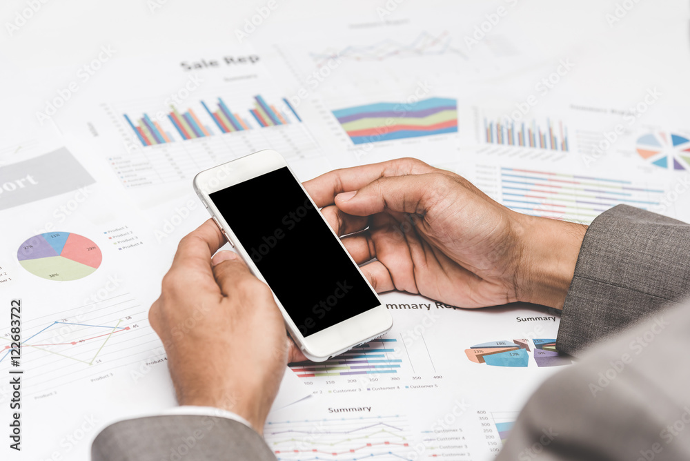 Businessman using smartphone mobile on the table with graph and chart sheet paper at office. Businessman using smartphone mobile on the table with graph and chart sheet paper at office.