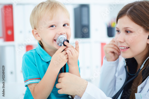Little boy plays with stethoscope during visit to a doctor.