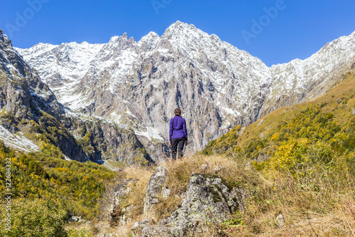 Young woman standing on stone and looking at snowy peak