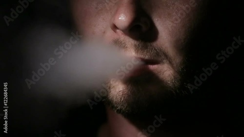 Young man smoking electronic cigarette on black background