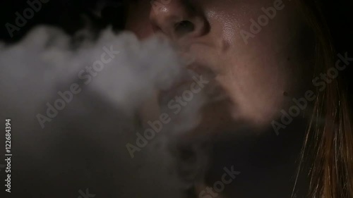 Young woman smoking electronic cigarette on black background
