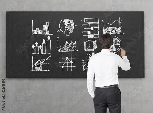 Businessman in white shirt is drawing diagrams on blackboard