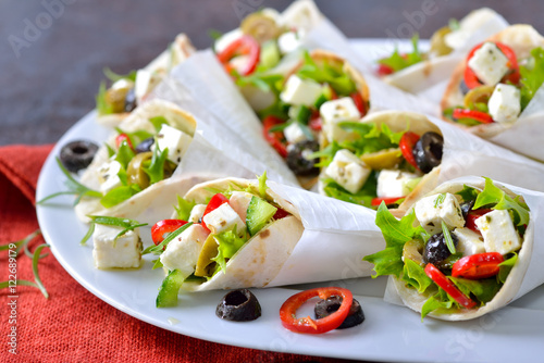 Mini-Tortillas gefüllt mit griechischem Bauernsalat mit Fetakäse sowie grünen und schwarzen Oliven - Mini wraps stuffed with Greek farmers salad with feta cheese and olives, served in white paper bags