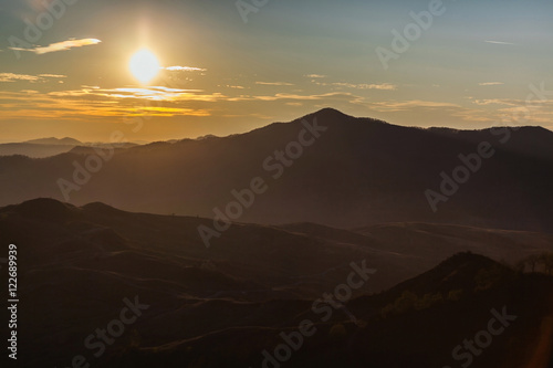 Sun low over silhouette of landscape