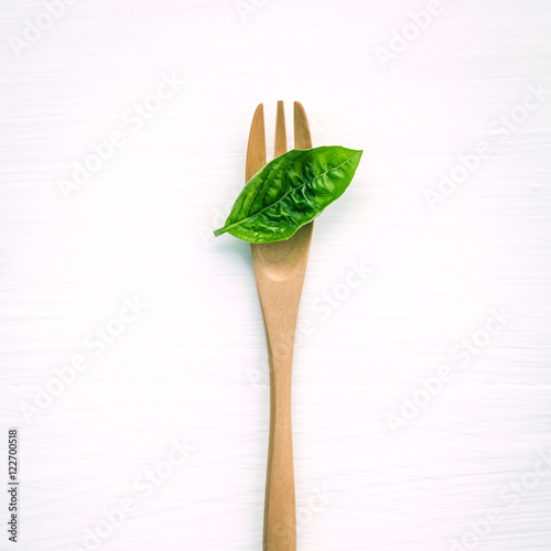 Closeup fresh sweet basil leaves with fork on white wooden bac