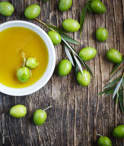 Fresh green olives with leaves and olive oil on wooden backgroun