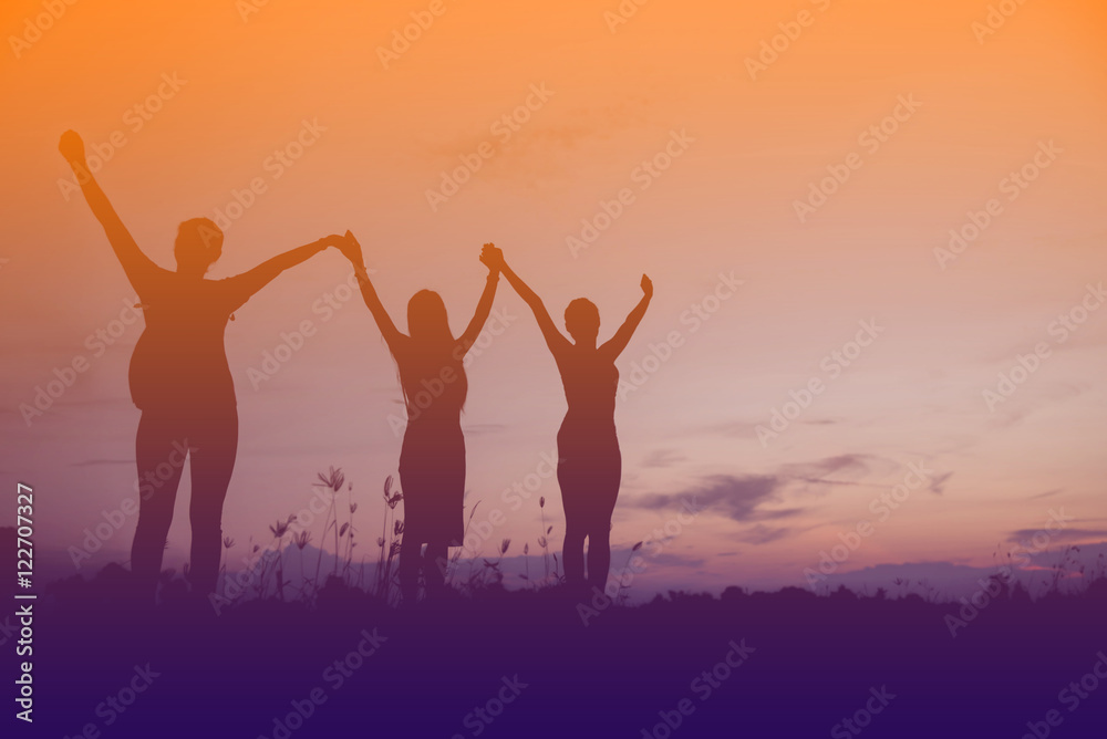 Friends holding hands up at sunset.