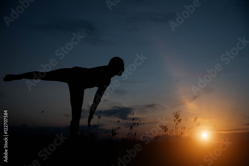 Silhouette of a young woman practicing yoga at sunset