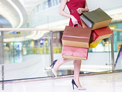 Bild auf Leinwand young woman carrying colorful paper bags walking in shopping mal