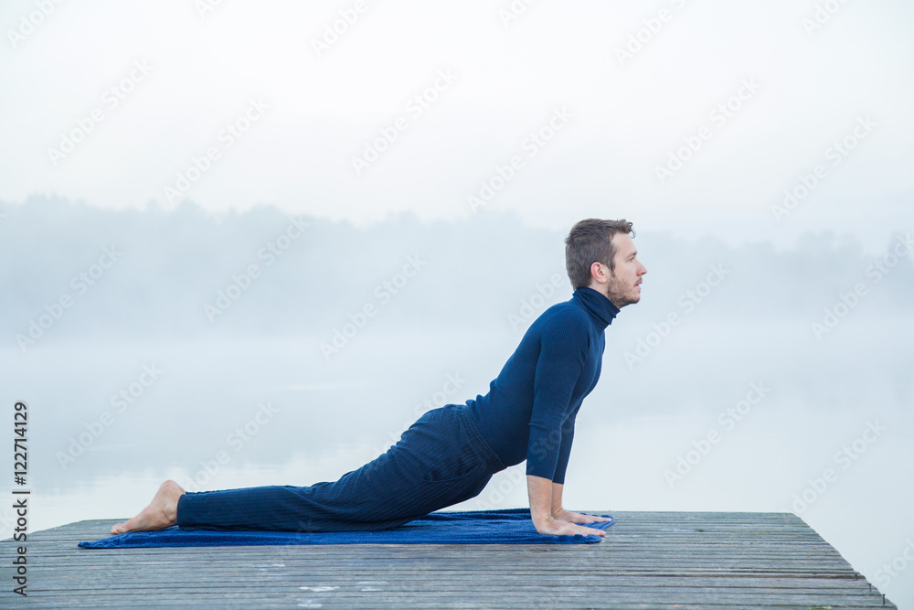 Man relaxing and practicing yoga in the mist on the lake footbridge early morning. Peaceful atmosphere. Foggy air.