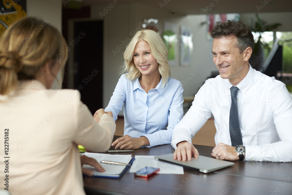 Handshake. Shot of an investment manager shaking hands with smiling woman while consulting with middle aged couple about financial savings. Handshake. Shot of an investment manager shaking hands with smiling woman while consulting with middle aged couple about financial savings.