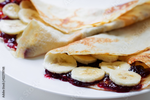 Thin pancakes with cherry jam and banana slices on a white plate