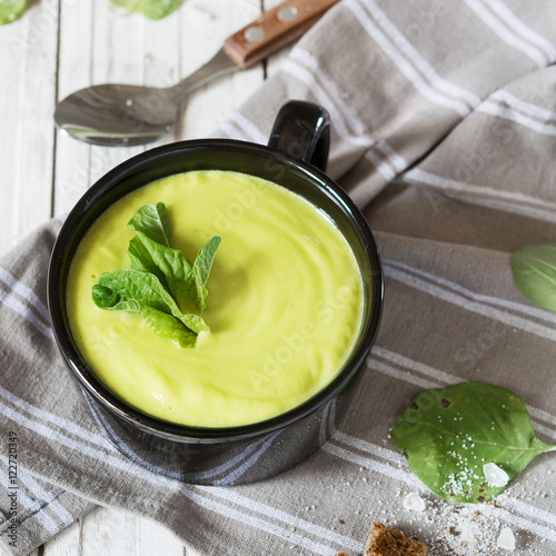 Avocado cream soup in the bowl on the rustic table.