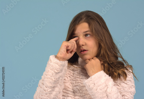 Girl rubbing her itchy eye against a blue background. The girl was ten years old (tween) when the photo was taken.