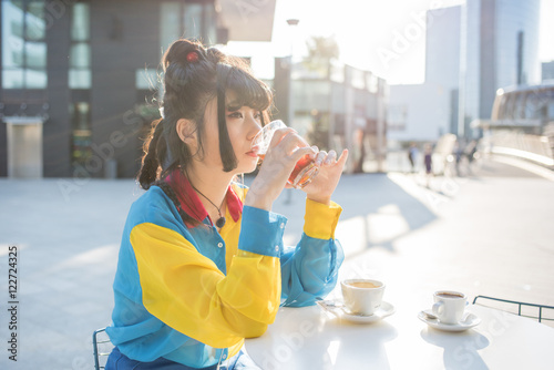 young beautiful asian millennial woman nonconformist sitting outdoor in a bar in city back light having a glass of drink, overlooking pensive - break, relaxing, happy hour concept photo