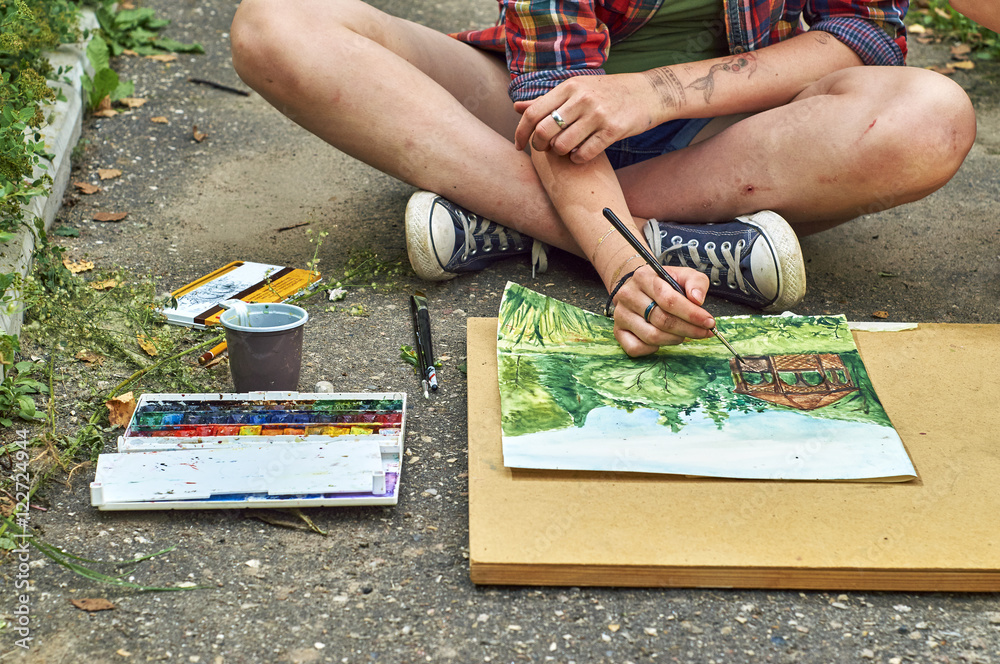Fototapeta premium Teenage girl is painting a watercolor picture sitting on the pavement 