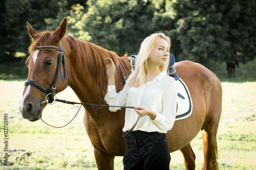 Молодая девушка со светлыми волосами стоит рядом с коричневой лошадью  © natasidorova 