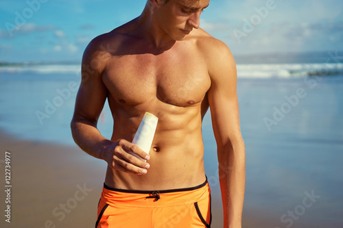 UV protection and suntan. Young handsome man holding bottle with sunscreen lotion on the sea beach.