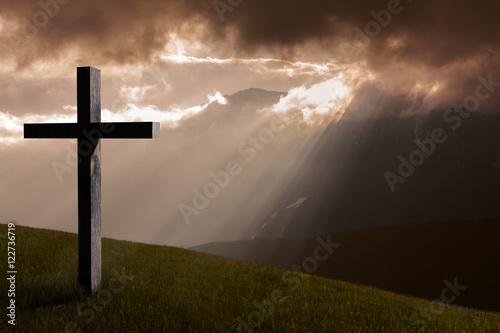 Jesus Christ cross. Christian wooden cross on a background with dramatic light, mountains, colorful sunset and orange clouds and sky.  Easter, resurrection, Good Friday concept