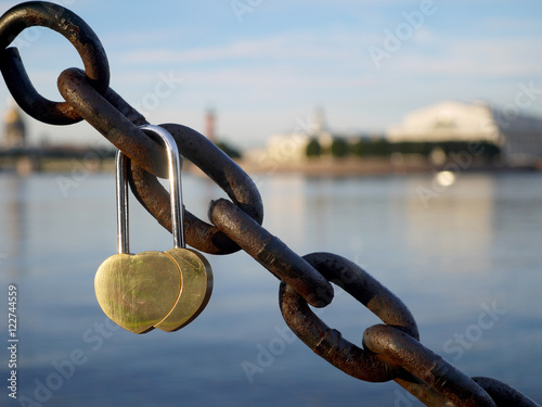 Double heart golden love lock on a rusted chain at Neva river embankment in St. Petersburg, Russia