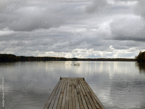 Wooden pier at Svir river. Cloudy sky mirroring in waters.