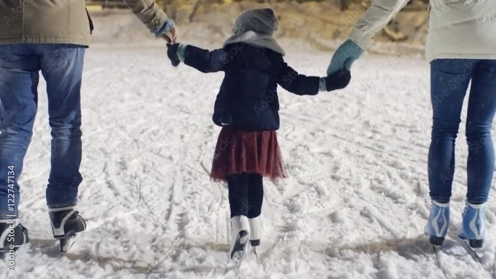 Following shot with rear view of young couple holding hands of little girl and skating on ice rink, then letting her go 