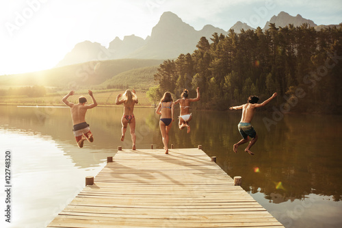 Group of young people jumping into the water from a jetty photo