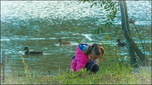 beautiful little girl playing in the park, looking stones. ducks on the lake