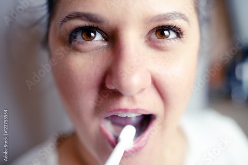 Closeup portrait of young woman brushes teeth in bathroom an electric brush