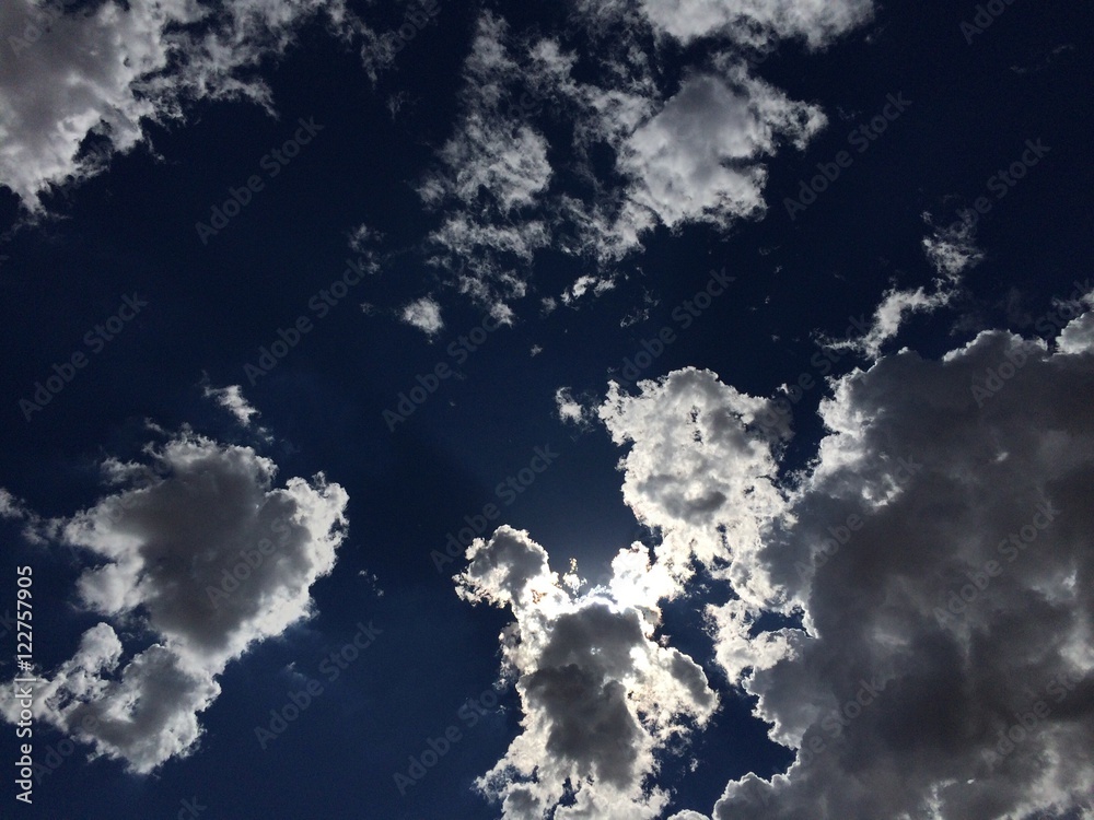 Beautiful blue sky with sun shining through white puffy clouds Beautiful blue sky with sun shining through white puffy clouds