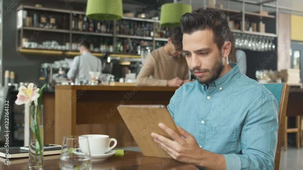 Hispanic Ethnicity Young Man using Tablet Computer at Cozy Coffee Shop. Shot on RED Cinema Camera in 4K (UHD). Hispanic Ethnicity Young Man using Tablet Computer at Cozy Coffee Shop. Shot on RED Cinema Camera in 4K (UHD).