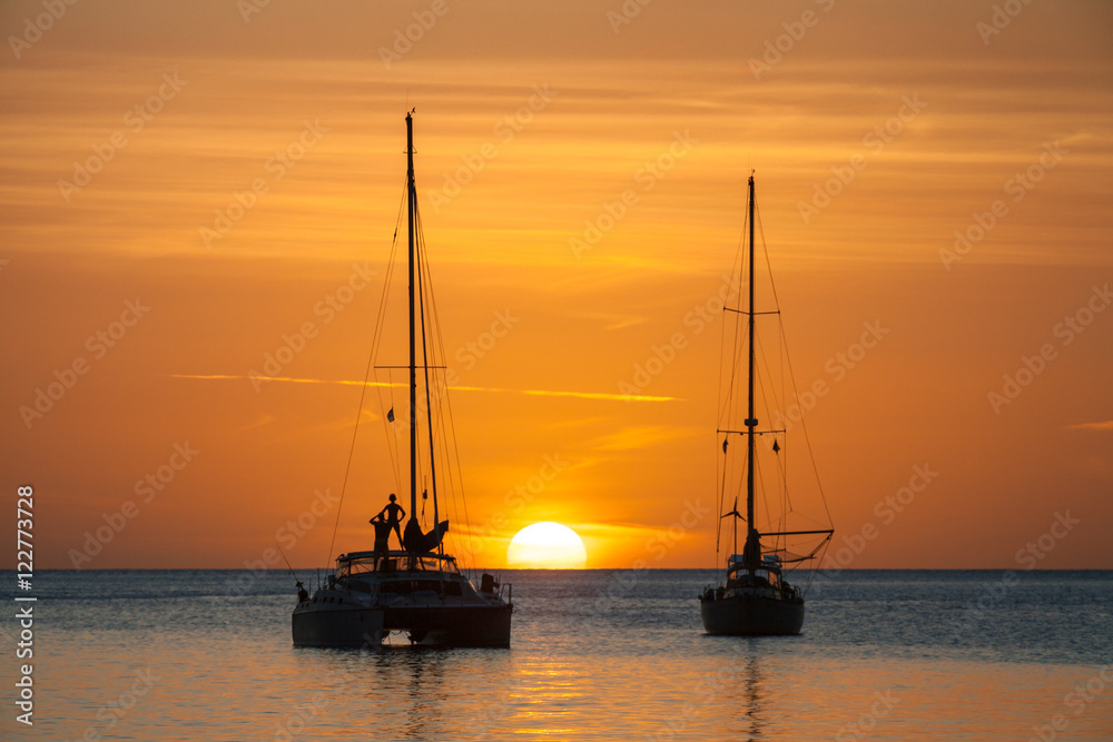 Fototapeta premium Słońce nad oceanem, osoba stojąca na żaglówce w sylwetce. Duże białe słońce na horyzoncie na Karaibach. Marigot Bay, St Lucia.