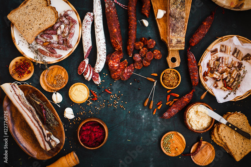 Overhead view of cured meats, sausage with mustard sauce on rustic dark table. 